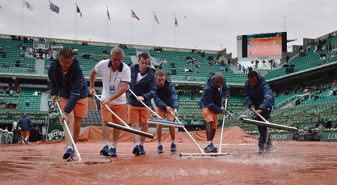 TOPSHOT - Workers sweep the water off from the tarp covering the central court at the Roland Garros 2016 French Tennis Open in Paris on May 22, 2016. / AFP / Eric FEFERBERG        (Photo credit should read ERIC FEFERBERG/AFP/Getty Images)