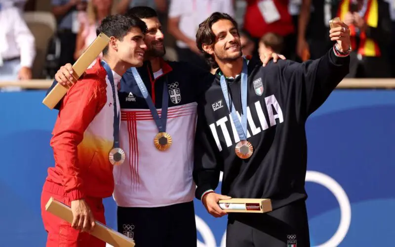 PARIS, FRANCE - AUGUST 04: Gold medallist Novak Djokovic of Team Serbia (C), Silver Medallist Carlos Alcaraz of Team Spain (L), and Bronze Medallist Lorenzo Musetti of Team Italy (R) pose for a selfie on the podium during the Tennis Men's Singles medal ceremony after the Tennis Men's Singles Gold medal match on day nine of the Olympic Games Paris 2024 at Roland Garros on August 04, 2024 in Paris, France. (Photo by Clive Brunskill/Getty Images)